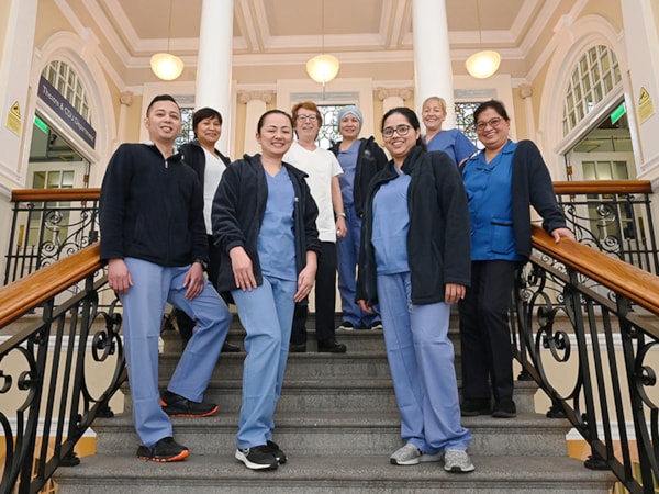 Group of female and male nurses standing on a staircase in a hospital smiling at camera